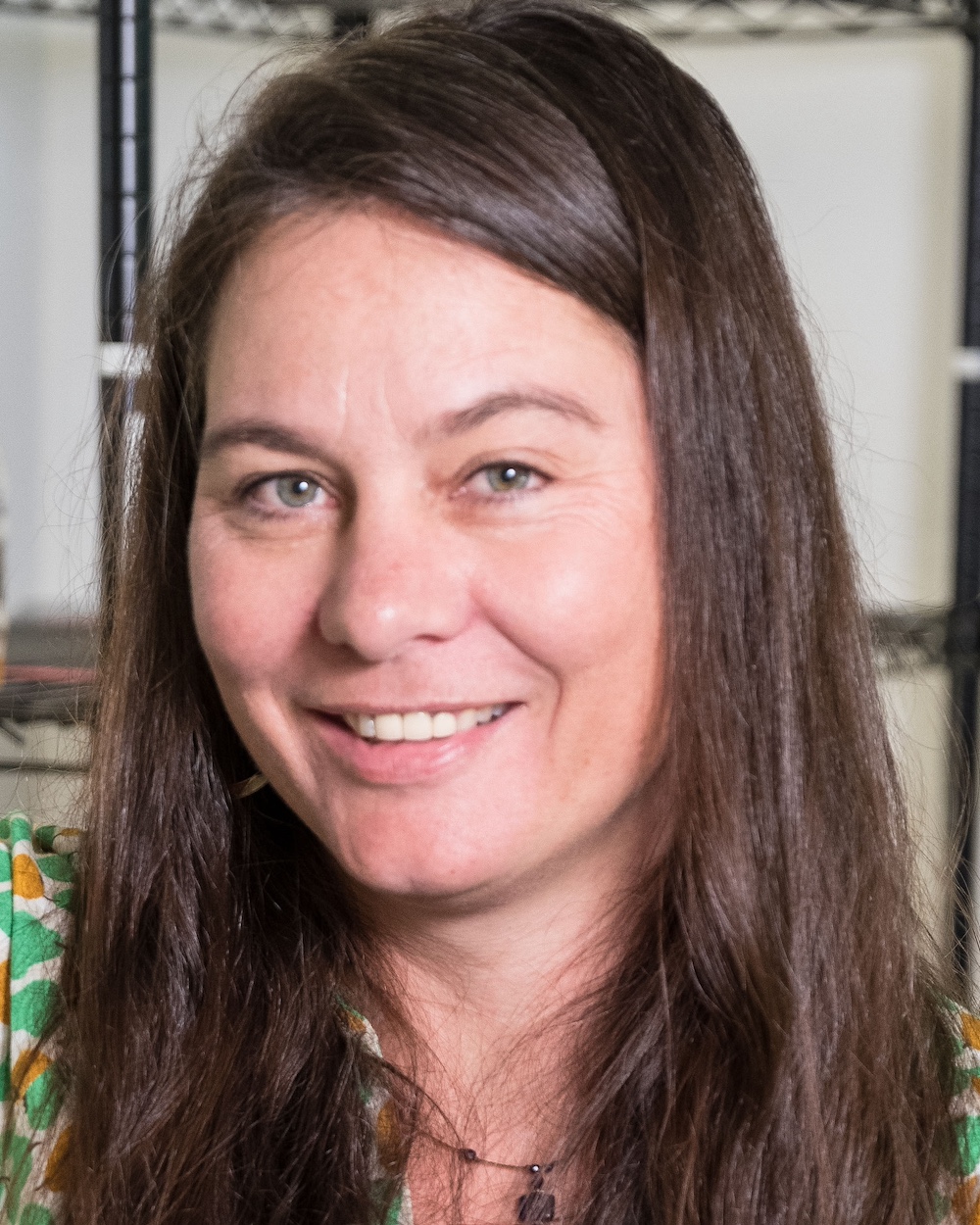 Angelicque smiles at the camera wearing a green patterned shirt and necklace.