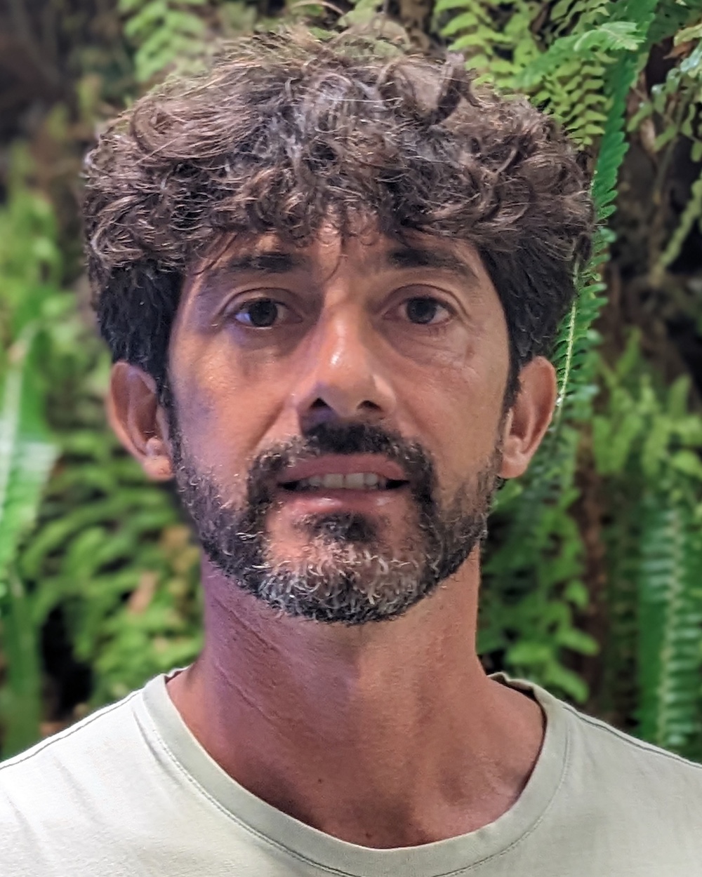 Benedetto faces the camera in front of lush vegetation.