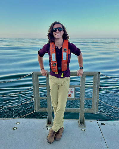 Hunter leans on a railing and smiles at the camera from the deck of a ship, wearing sunglasses and an orange life vest.