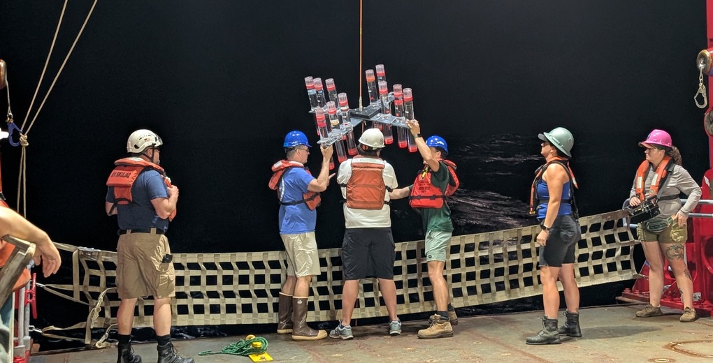Three scientists work together to lift a sediment trap array over the edge of the ship.