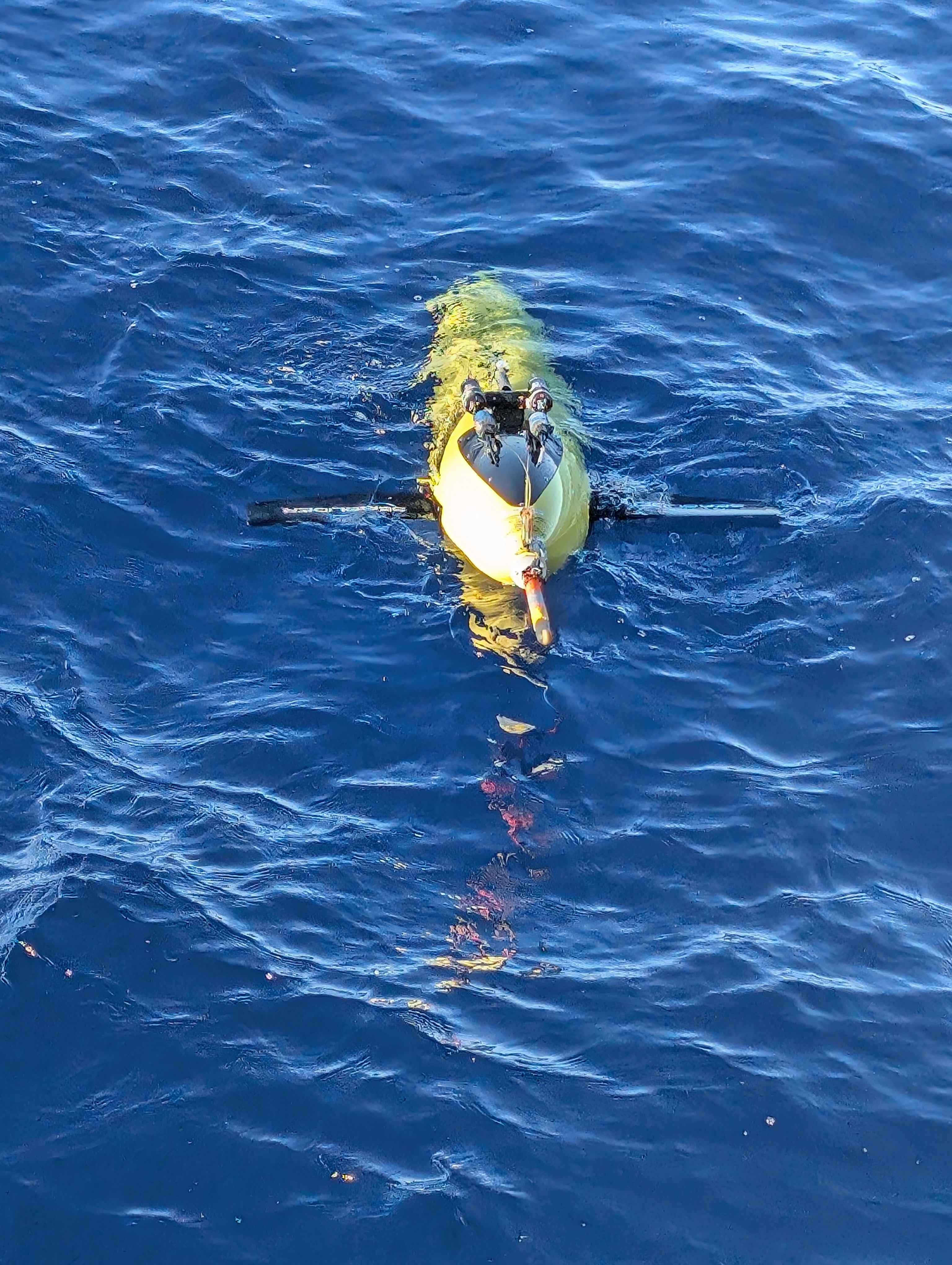 A yellow Seaglider sits at the surface of bright blue water, ready to start collecting data.
