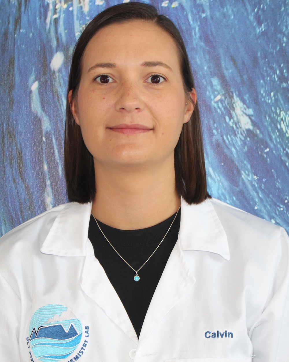 Calvin poses in front of a blue background wearing a black shirt and white lab coat.