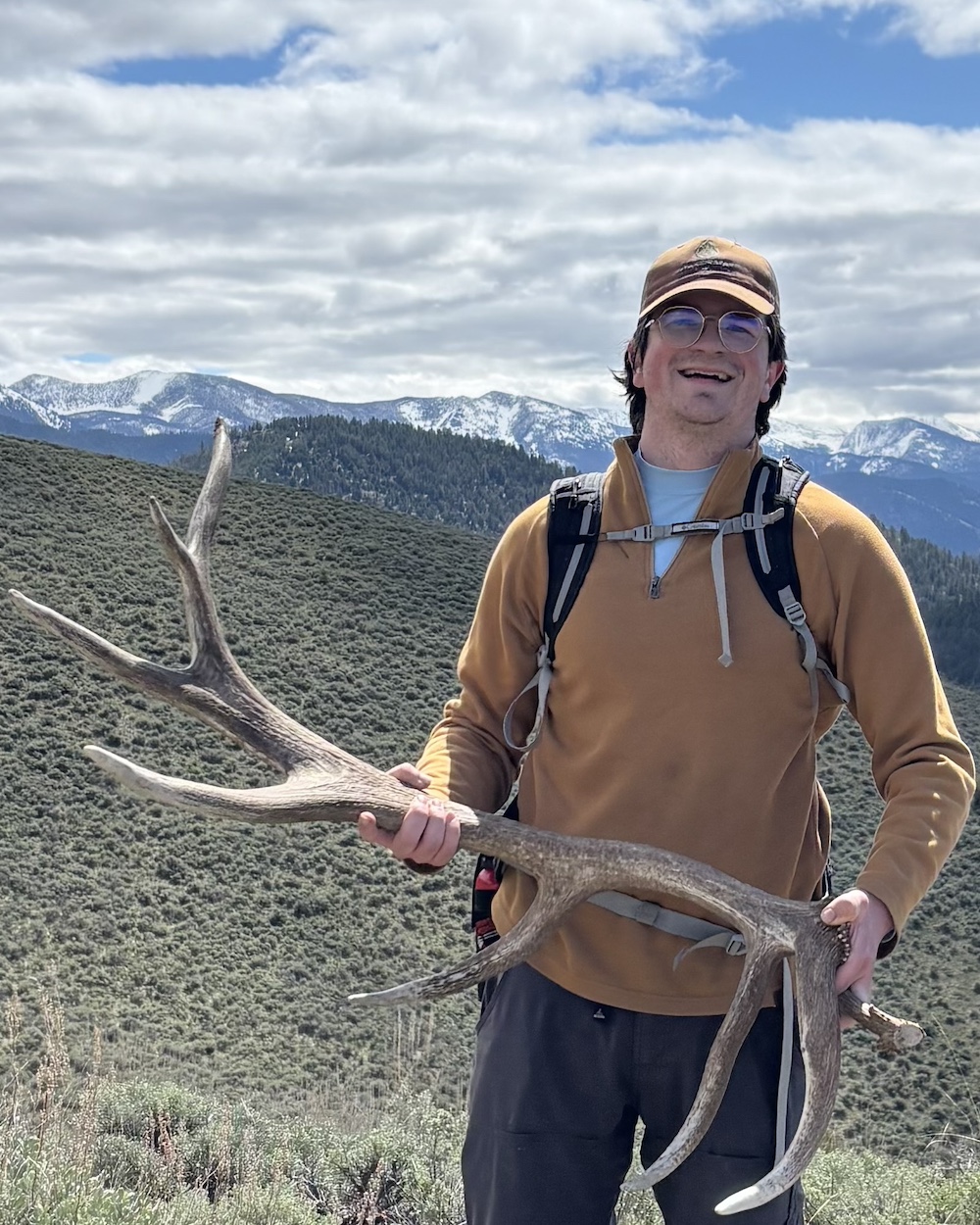 Jared grins while holding an antler in front of a mountainous landscape.