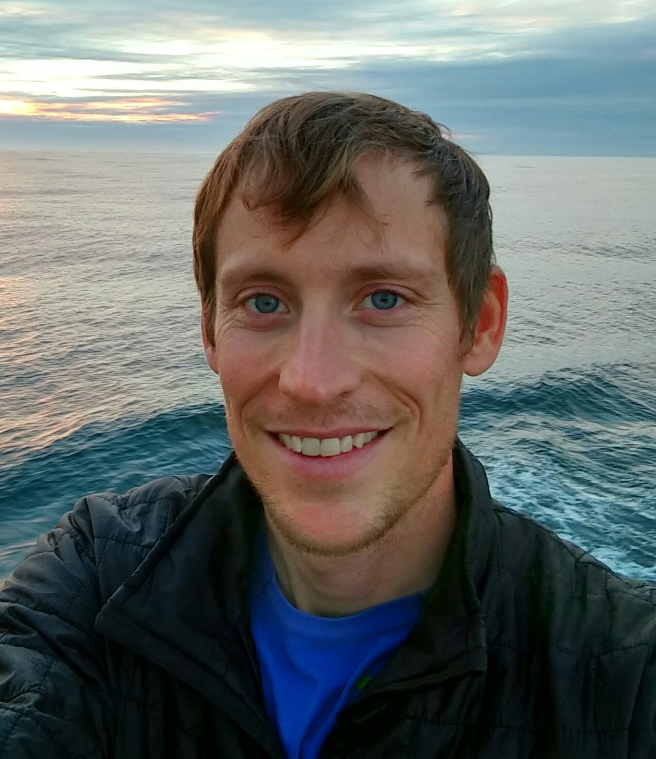 Tully smiles in front of the ocean at sunset.